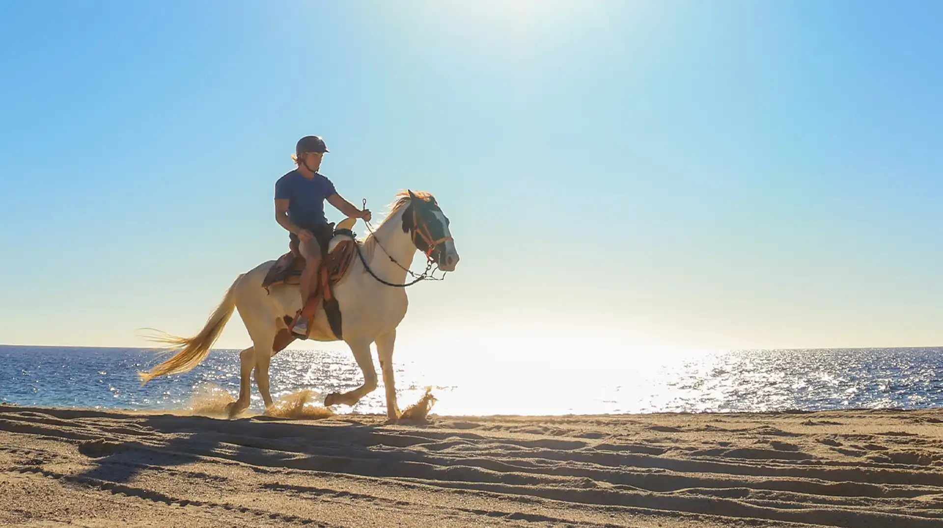 Hombre montando a caballo en la playa de Los Cabos al atardecer.
