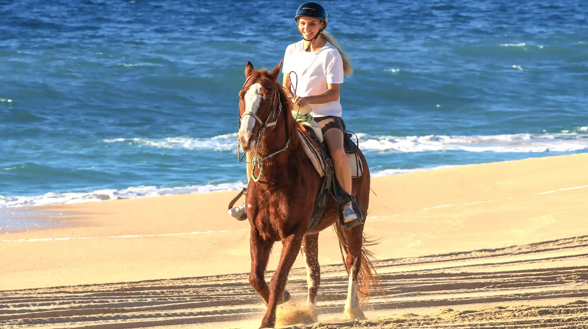 Mujer montando a caballo en la playa de Los Cabos junto al mar.
