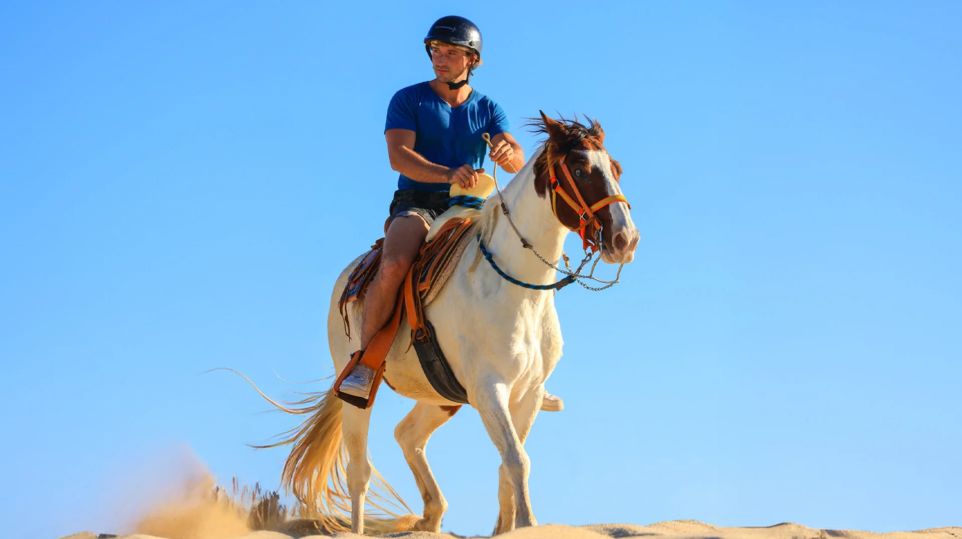 Hombre montando a caballo en las dunas de arena en Los Cabos.