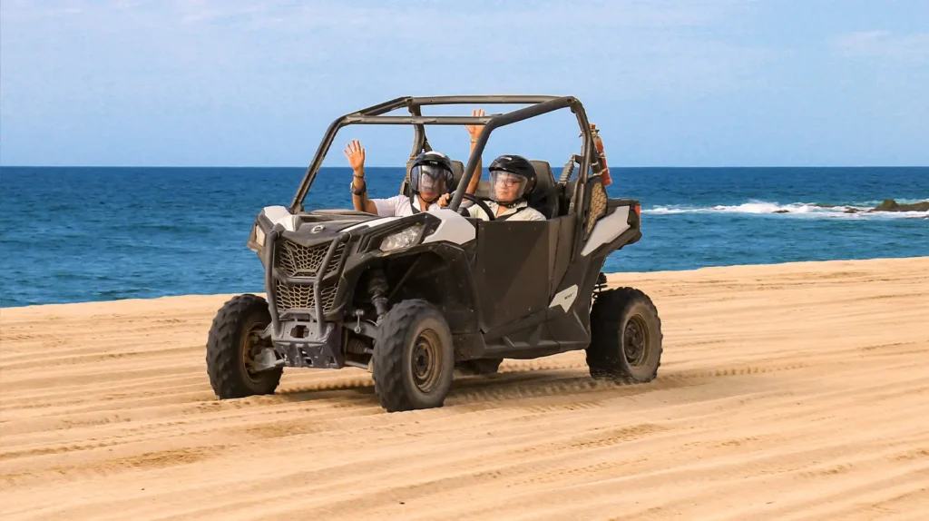 Dos personas conduciendo un UTV Side by Side sobre la playa en Los Cabos con el mar azul al fondo