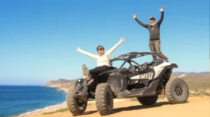 Pareja celebrando sobre Can-Am Maverick X3 con vista al océano en tour off road en Los Cabos
